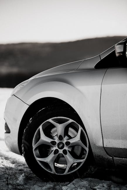 A monochrome close-up of a car wheel on a snowy landscape, highlighting winter conditions.
